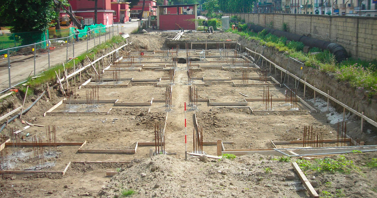 Cantiere con fondazioni in cemento ed edificio in costruzione.